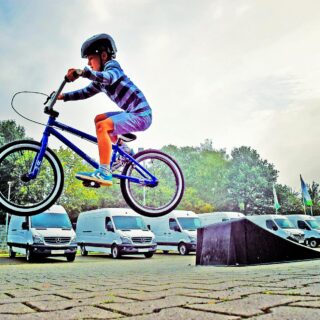 boy in black nutshell helmet on blue bmx bike having hangtime after taking off on ramp